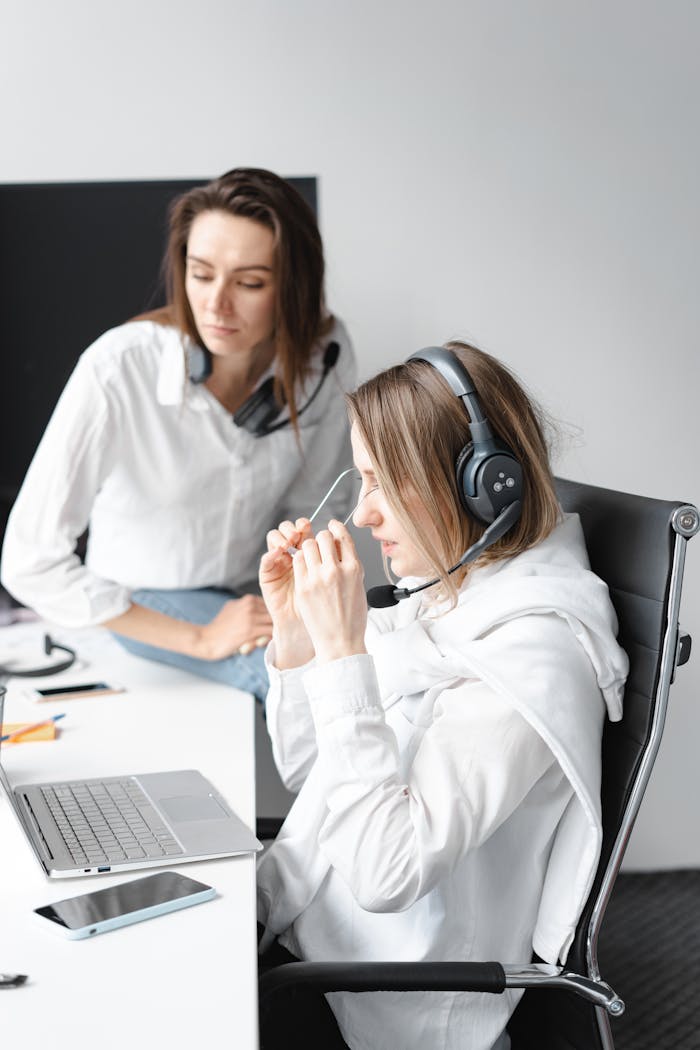 Two female customer service agents discussing work at their desk with headsets.