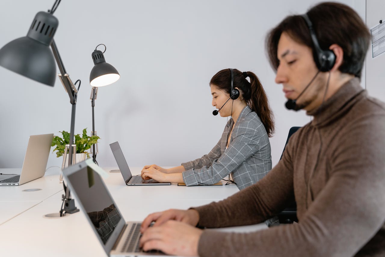 Business professionals working in a call center, wearing headsets and using laptops.